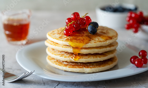 Pile of pancakes with red currants, blueberries and honey on a grey plate with fork