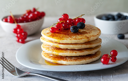 Pile of pancakes on a grey plate with red currants, blueberries and fork