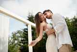 passionate man embracing cheerful woman in white beach wear on luxury resort during vacation