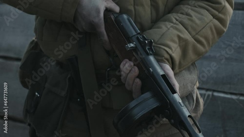 Medium close-up of unrecognizable officer standing in trench taking safety off his rifle, WW2 reenactment photo