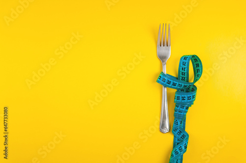 Diet, weight loss and weight loss concept. Fork with measuring tape on yellow background, top view, space for text photo