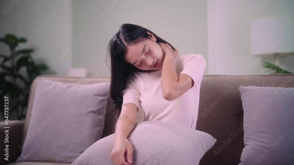 An Asian woman do self massage at her neck and sitting in the wrong position on the sofa at home, People with body-muscles problem and health care concept. An Asian woman do self massage at her neck and sitting in the wrong position on the sofa at home, People with body-muscles problem and health care concept.