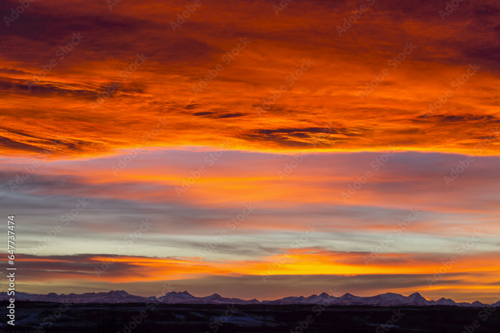 Dramatic Fiery Sunset With Orange And Red Clouds And Mountains In The Distance; Calgary, Alberta, Canada Dramatic Fiery Sunset With Orange And Red Clouds And Mountains In The Distance; Calgary, Alberta, Canada