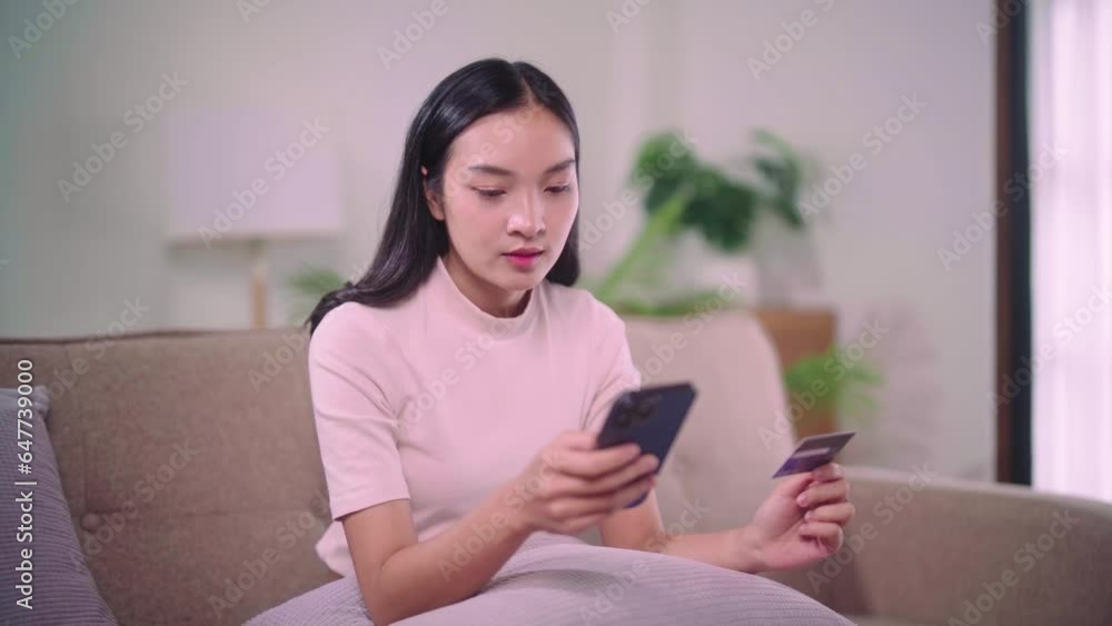 Dreamy asian woman with smartphone and credit card sitting on couch pay electronic money in internet online remote shopping or check bank account balance provide distant payment. Dreamy asian woman with smartphone and credit card sitting on couch pay electronic money in internet online remote shopping or check bank account balance provide distant payment.