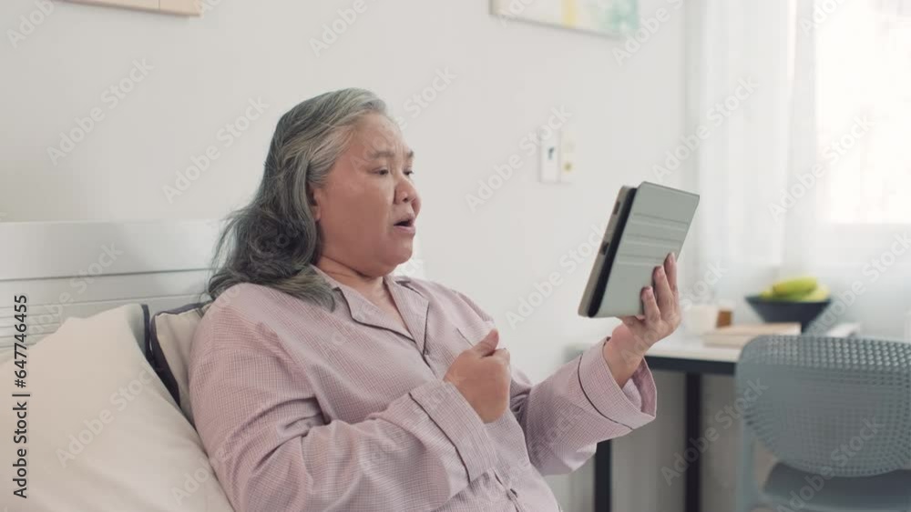Medium shot of old woman in pajama talking to her children on video call on digital tablet while resting in bed