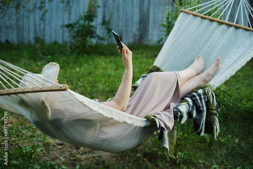 Embracing Slow Living: Woman Finds Solitude in Backyard Hammock, Smartphone in Hand for a Mindful Escape photo