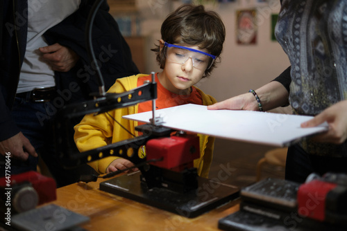 Hands-On Learning: In a sunlit workshop, a boy is engrossed in mastering the art of woodturning, as his attentive instructor stands by, ensuring both safety and skill development.