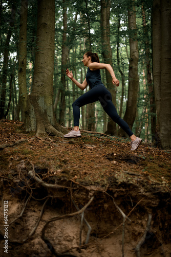 Beautiful view of fitness female athlete running uphill on forest path in summer day