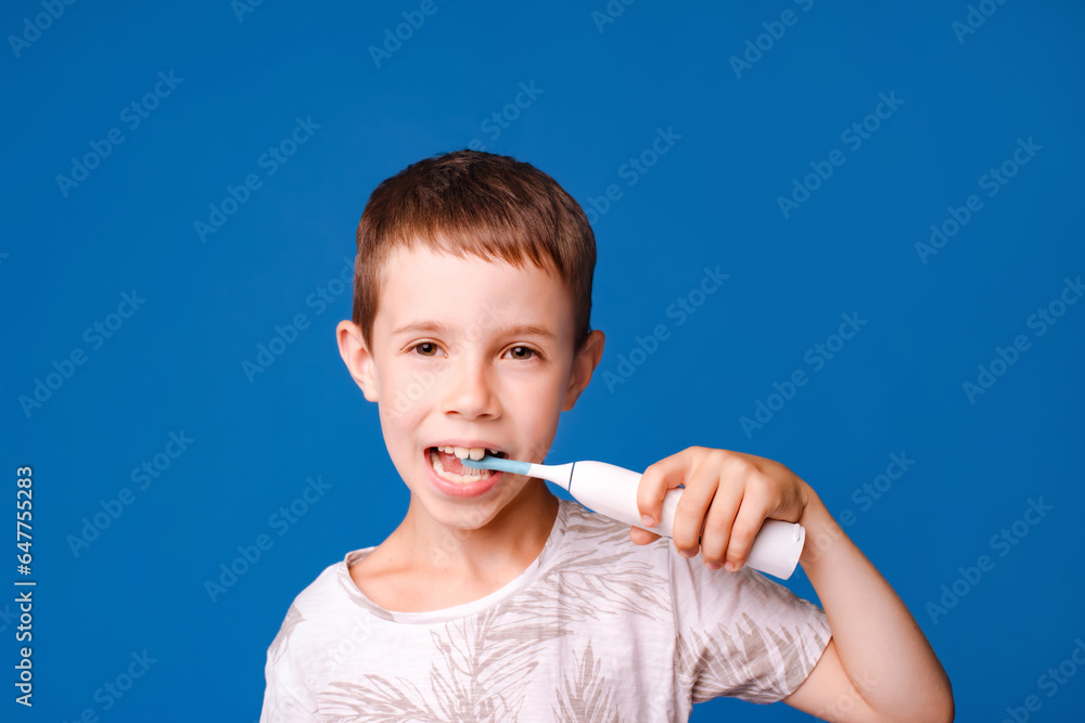 child boy brush teeth with electric toothbrush looking at camera isolated over light blue studio background child boy brush teeth with electric toothbrush looking at camera isolated over light blue studio background