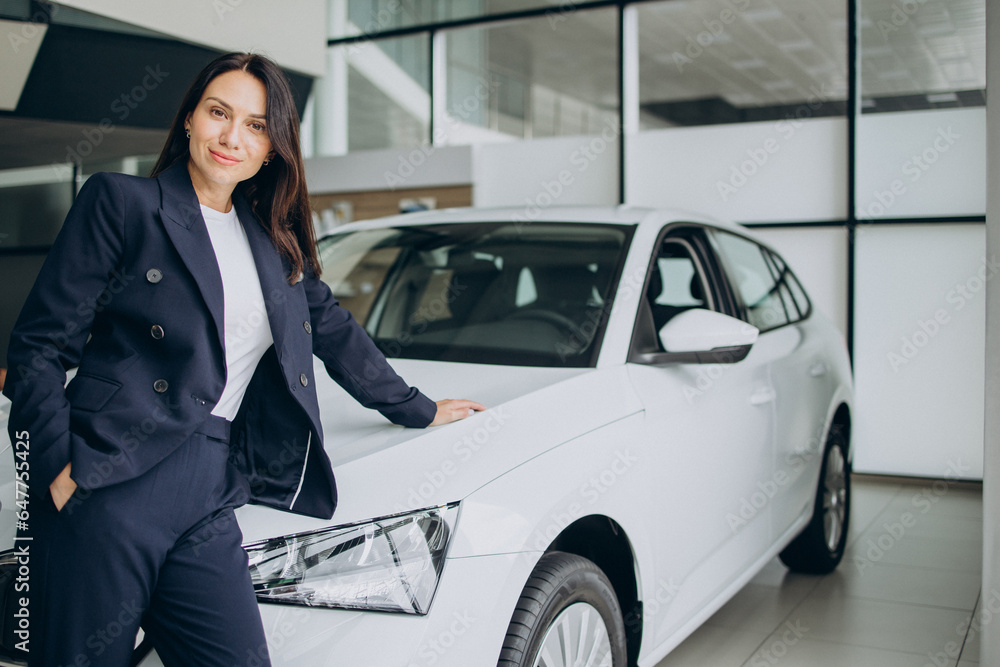 Sales woman in a car showroom standing by white car