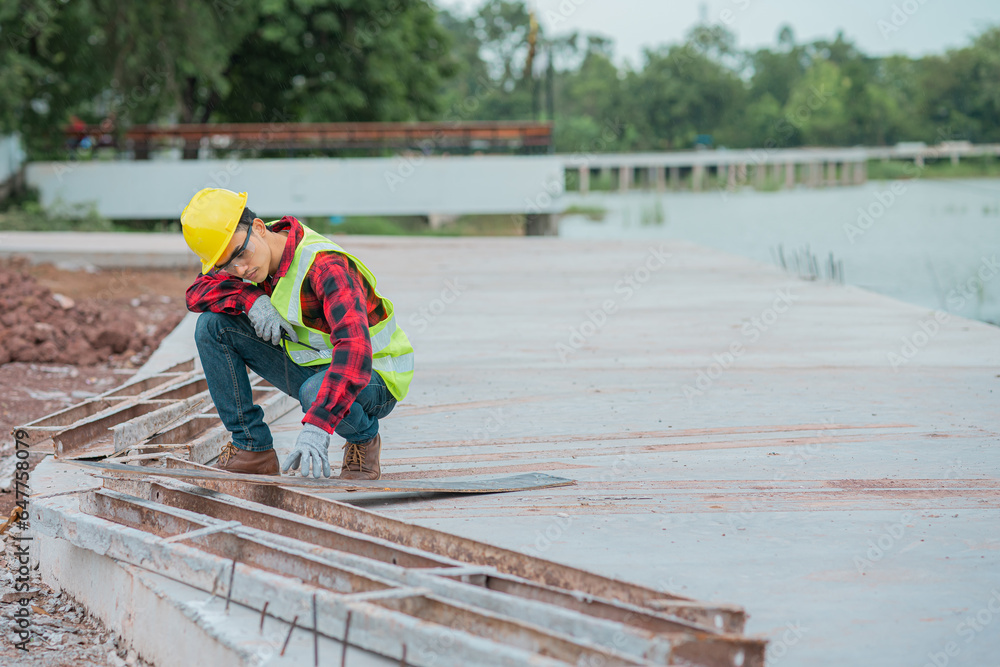 An engineer wearing a yellow hat, red shirt and green outerwear carries a radio at the construction site. An engineer wearing a yellow hat, red shirt and green outerwear carries a radio at the construction site.