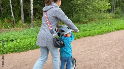 mother and toddler child little boy ride a scooter in the park. Aleksandrovsky Park, Pushkin, St. Petersburg, Russia. photo