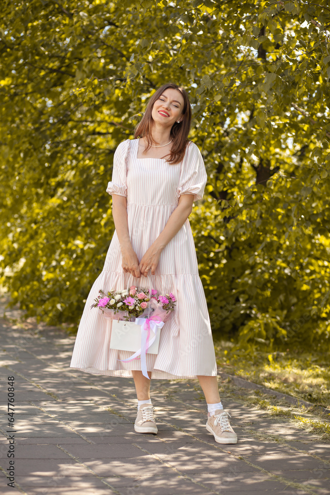 Beautiful girl with flowers, in a dress, glasses and sneakers. A beautiful bouquet of flowers in a box in the hands of a beautiful girl who walks along the street on a sunny day. Beautiful girl with flowers, in a dress, glasses and sneakers. A beautiful bouquet of flowers in a box in the hands of a beautiful girl who walks along the street on a sunny day.