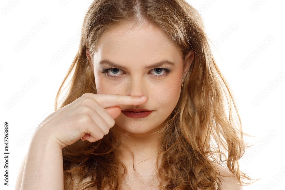Beautiful blonde woman hold a finger under her hose on a white background Beautiful blonde woman hold a finger under her hose on a white background
