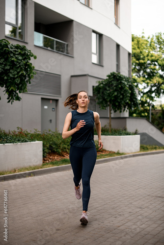 Front view of active sporty young woman running on urban street in morning.