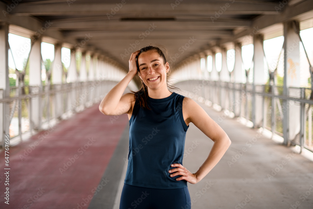 Φωτογραφία Outdoor shot of cheerful sporty woman dressed in activewear standing on bridge,