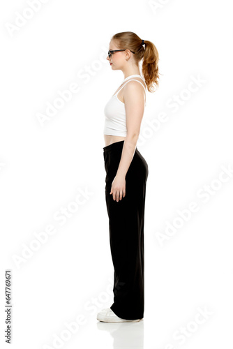 Side view of young blond woman in trousers and white blouse standing on white background