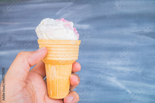 One person's hand holds a pastel ice cream cone very sweet blue background. The pink ice cream mobile figure leaves space for calligraphy. © singjai