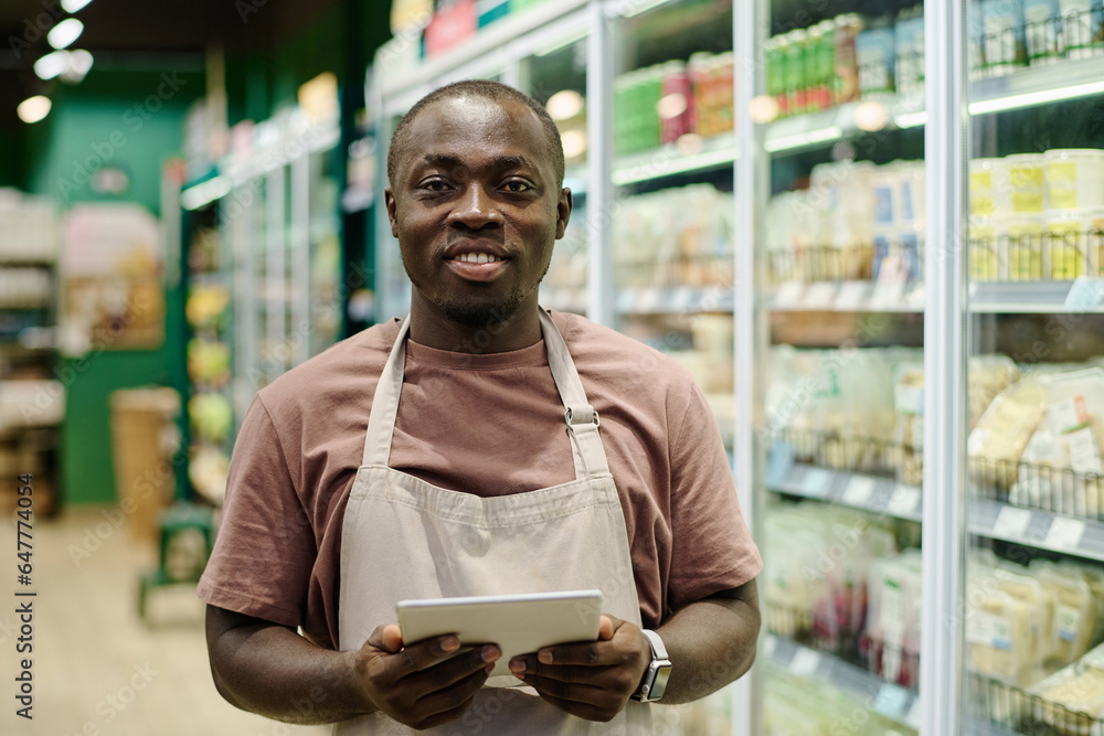 Portrait of African American supermarket worker smiling at camera while controlling work with tablet pc Portrait of African American supermarket worker smiling at camera while controlling work with tablet pc