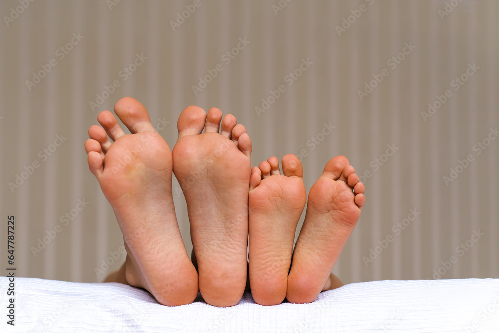 Fototapeta premium Small and large bare feet, two pairs of barefoot close-up, children lying on the bed. Foot Relaxing. Togetherness and Growing up concept. Childhood moments