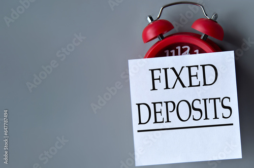 FIXED DEPOSITS - words on a white piece of paper on a gray background. Red alarm clock with white piece of paper photo