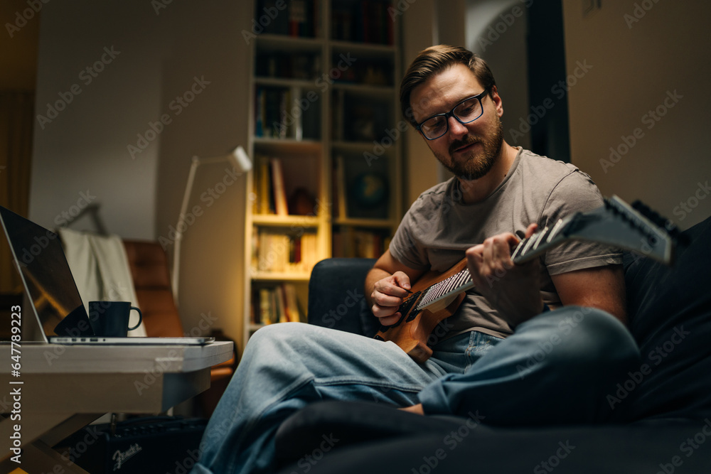 Caucasian man practicing guitar at home alone.