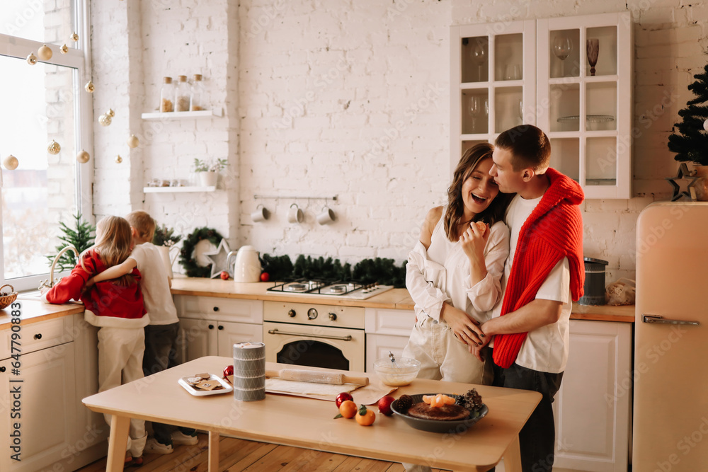 The concept of Christmas. A family with two children in sweaters prepare a festive food in the decorated kitchen in the house on a holiday. Two parents with their daughter and son have fun at home The concept of Christmas. A family with two children in sweaters prepare a festive food in the decorated kitchen in the house on a holiday. Two parents with their daughter and son have fun at home