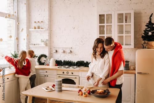 The concept of Christmas. A family with two children in sweaters prepare a festive food in the decorated kitchen in the house on a holiday. Two parents with their daughter and son have fun in the apar photo