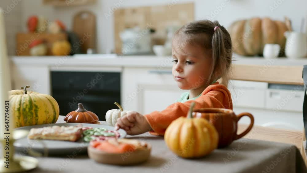 Happy Halloween! Little cute girl eating in the kitchen. Toddler girl in a pumpkin costume eating sandwiches on breakfast. Morning at home. Happy Halloween! Little cute girl eating in the kitchen. Toddler girl in a pumpkin costume eating sandwiches on breakfast. Morning at home.
