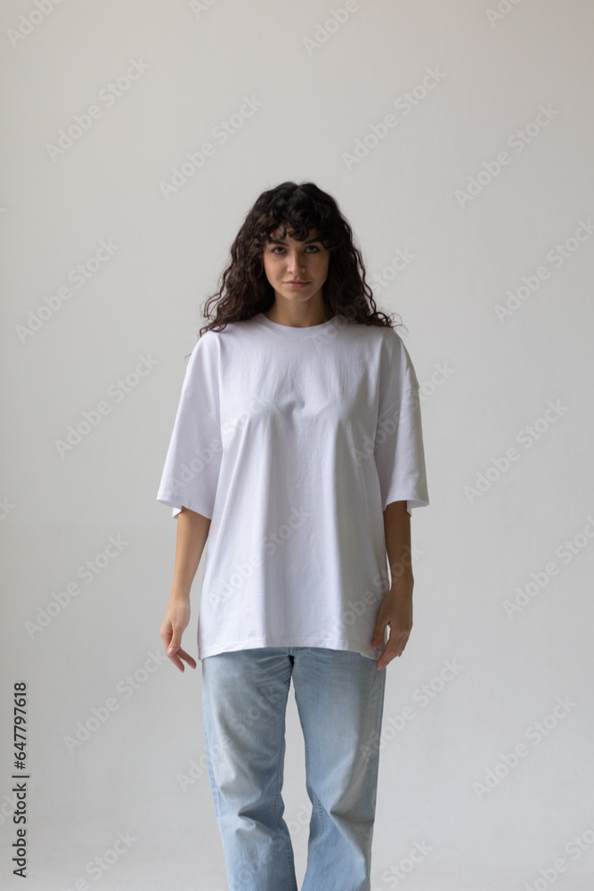 Beautiful brunette with curly hair in a white t-shirt and oversized jeans. Mock-up. Beautiful brunette with curly hair in a white t-shirt and oversized jeans. Mock-up.