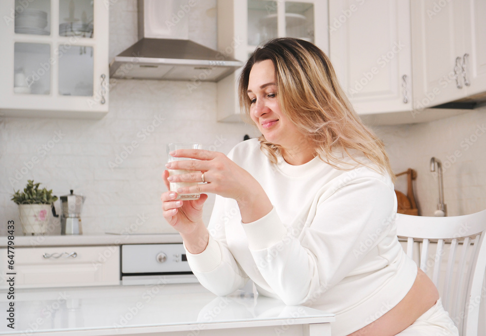 Beautiful pregnant woman in white suit is drinking milk in light kitchen. Beautiful pregnant woman in white suit is drinking milk in light kitchen.