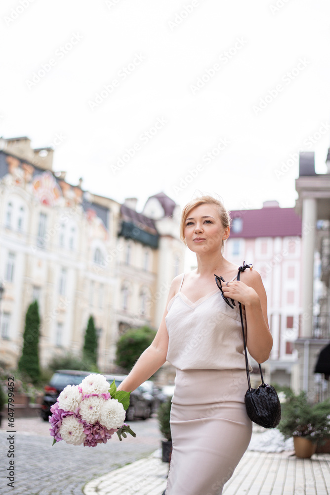 Fototapeta premium Young romantic girl on a first date with a bouquet of flowers on the city streets