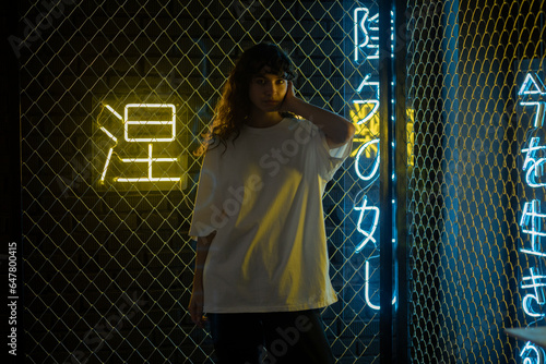 Attractive woman with curly hair in a white oversized t-shirt stands against the background of neon signs. photo