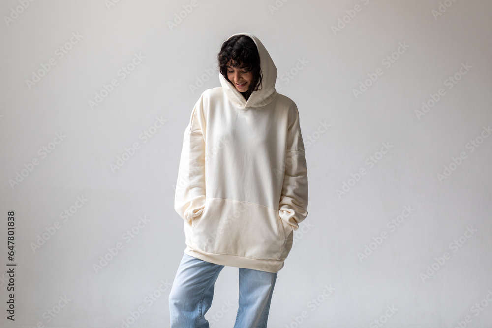 Brunette woman with curly hair in a white oversized hoodie and blue jeans. Brunette woman with curly hair in a white oversized hoodie and blue jeans.