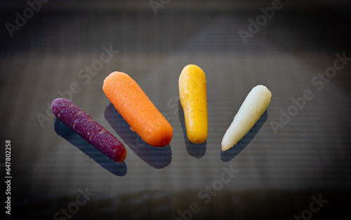 Pilled mini carrots in white, orange, yellow and dark purple colors placed on reflective background photo
