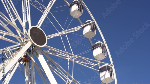 modern ferris wheel with closed cabins at carnival with blue sky no clouds in the background illuminated wide angle close up shot