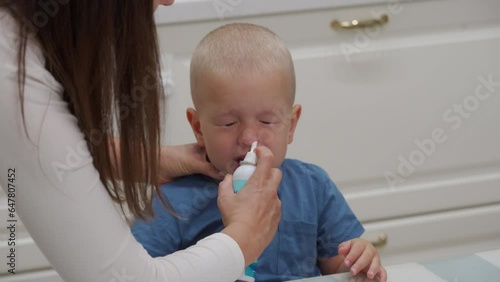 mother spraying nasal saline solution in the nose of her toddler child little boy is cold and has runny nose