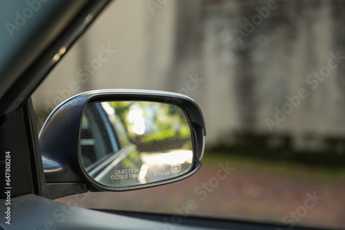 car\'s rearview mirror, reflecting a scenic road behind. The mirror symbolizes nostalgia, reflection, and the journey of life, capturing moments from the past