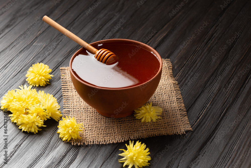 Honey with a dipper in a clay bowl and flowers on a dark wooden background. Honey with a dipper in a clay bowl and flowers on a dark wooden background.