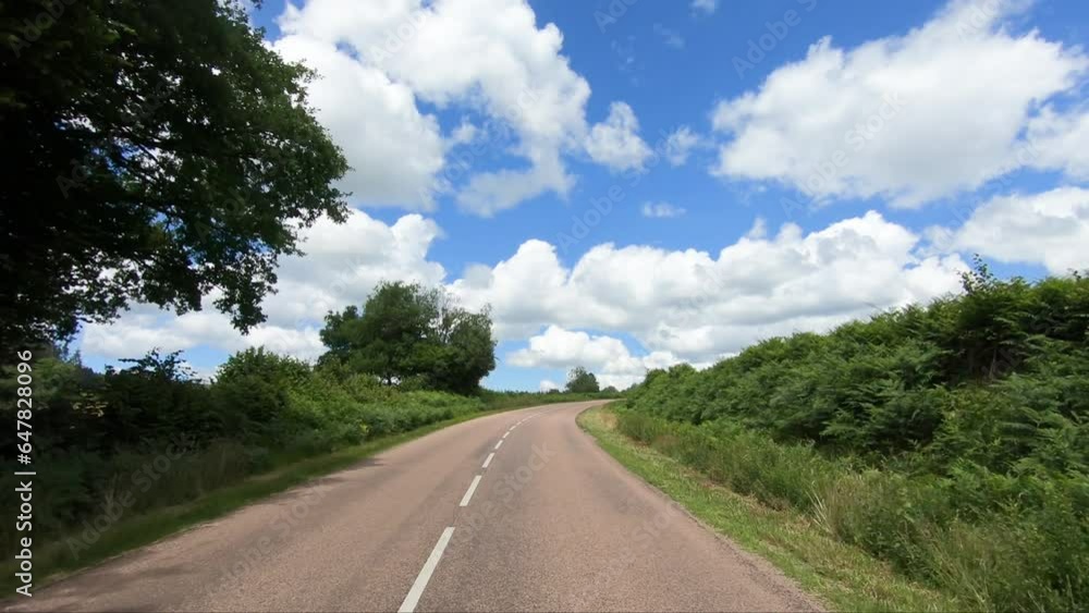 A road winds through the green countryside and its wheat fields in Europe, France, Burgundy, Nievre, towards Chateau Chinon, in summer, on a sunny day. A road winds through the green countryside and its wheat fields in Europe, France, Burgundy, Nievre, towards Chateau Chinon, in summer, on a sunny day.