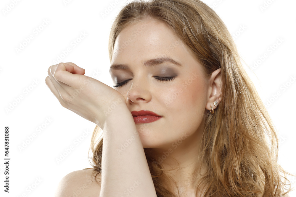 Beautiful young woman smelling aroma of parfume on her wrist on a white background Beautiful young woman smelling aroma of parfume on her wrist on a white background