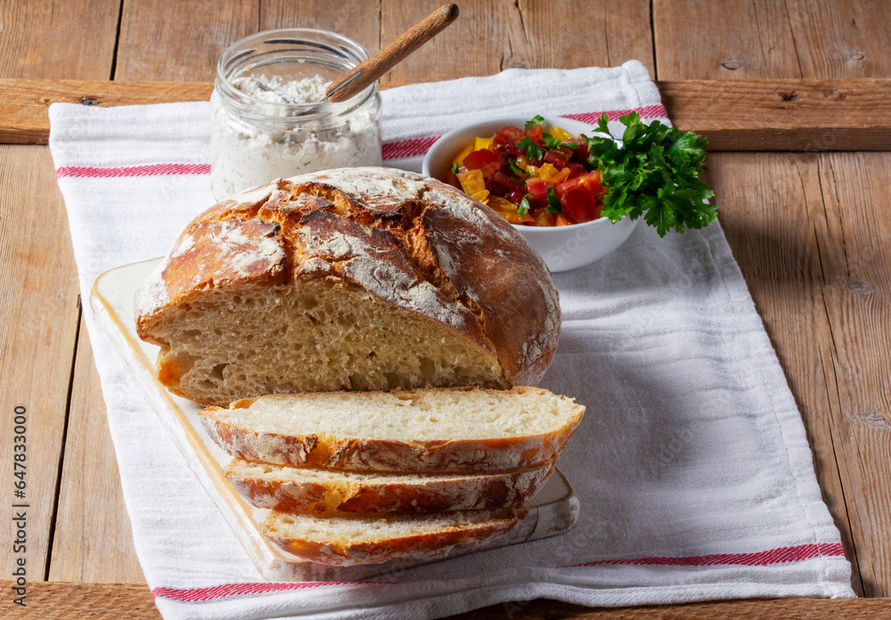 Round yeast bread made from white and whole grain flour, tomato salad and pate on a wooden background. Rustic style.