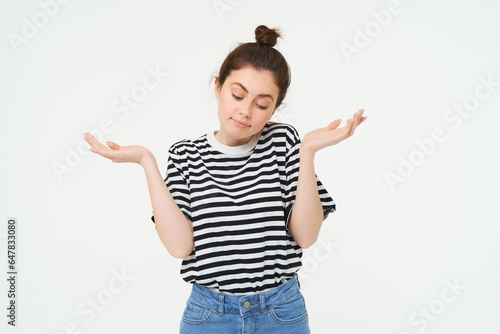 I dont know. Clueless young woman shrugging shoulders, looks confused, stands against white studio background photo