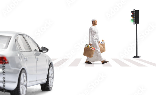 Car driving and a man in ethnic clothes walking and carrying grocery bags at a pedestrian crosswalk