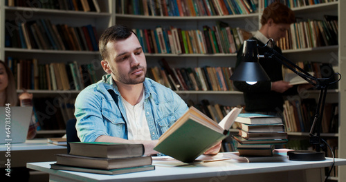 Caucasian young man working with old books in library and taking notes. Male student searching information in textbooks in bibliotheca. Education concept. Writing down data after search.