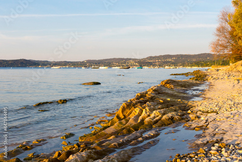Morning rest on Lake Garda in Italy. Due to the low water level rocks and stones stick out. In the background the red, blue and purple sky, calm water, boats, buoys and the shore in the morning light