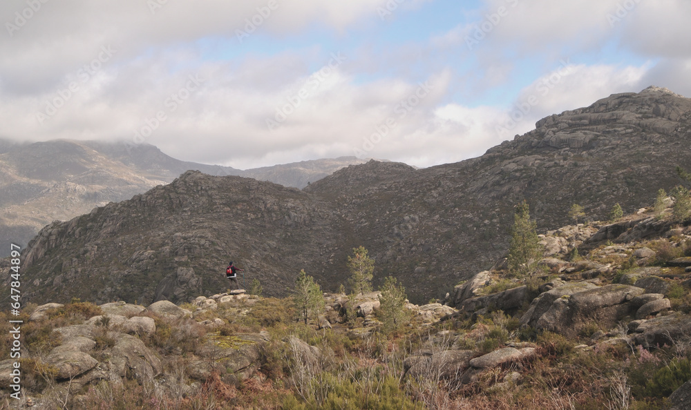 Woman hiking a mountain trail standing on top of a rock observing the beauty of a mountain range Woman hiking a mountain trail standing on top of a rock observing the beauty of a mountain range