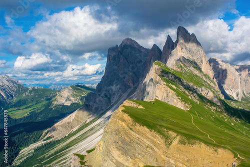 A breathtaking view of the Odle-Geisler Group in the Dolomites of South Tyrol, Italy. Backdrop of blue sky and white clouds complements the mountain range with picturesque rocks and covered in grass