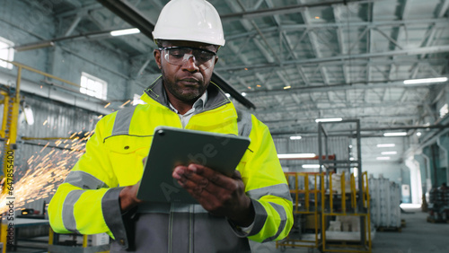 African american engineer works with tablet in production. Employee develops new important project plan. Male is developing new strategy for improving manufacturing department.