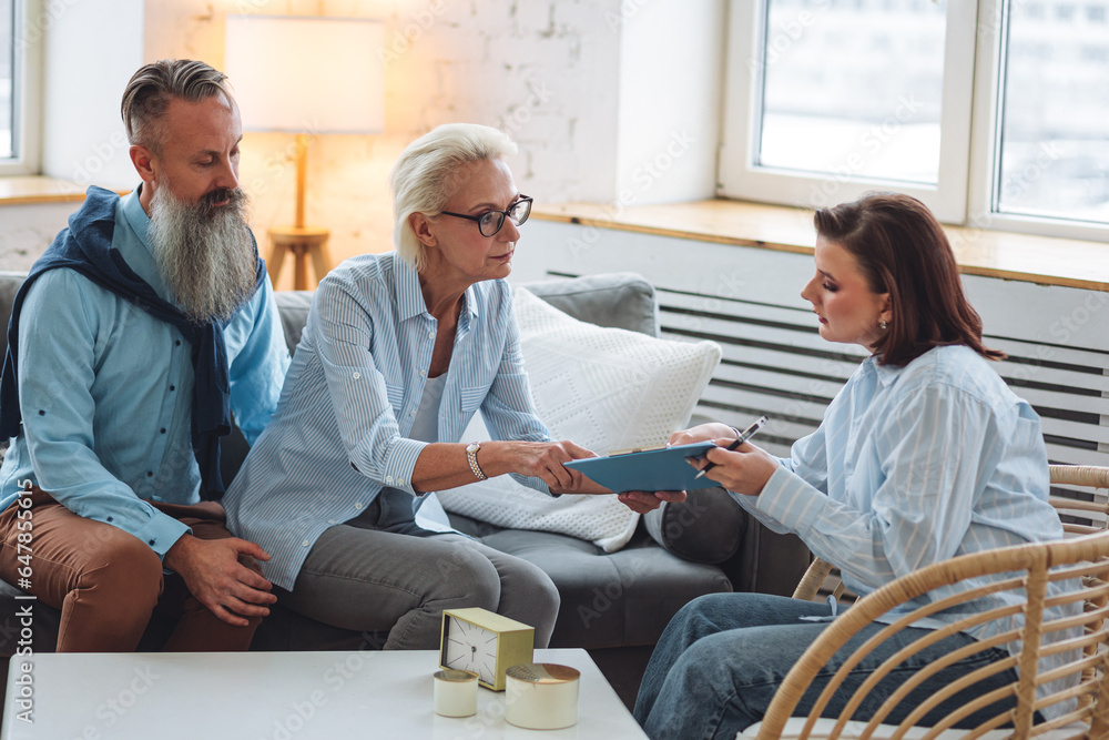 Fototapeta premium Psychologist cabinet. Female professional therapist at the session with senior mature retired couple, discussing mental health problems, depression. Concept of support, family relationships